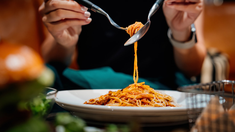 Person with plate of spaghetti, twirling pasta on fork with spoon