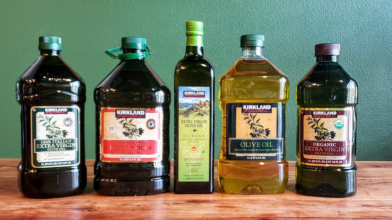 5 different Costco Kirkland Signature brand olive oils on a wood table.