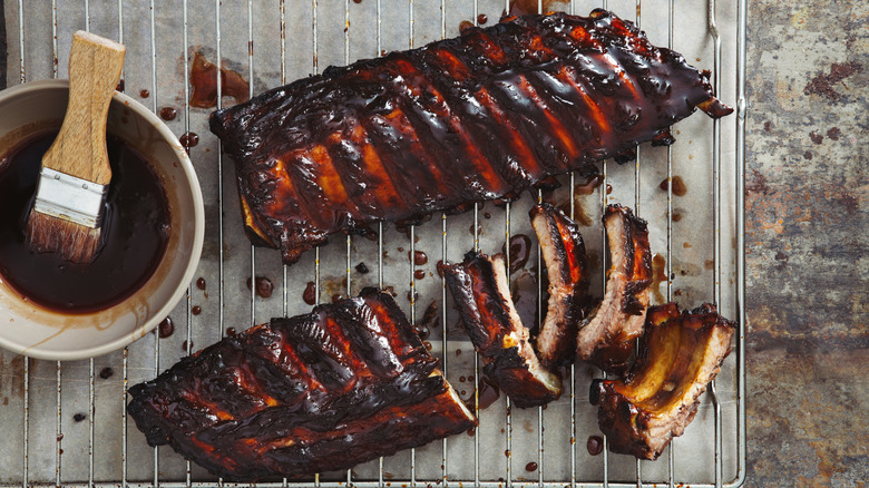 Two racks of BBQ rips on a wire rack next to a bowl of BBQ sauce