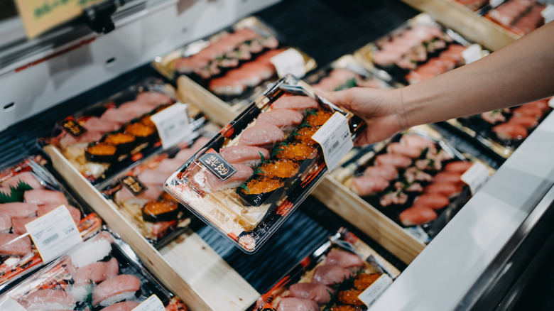Hand holding a sushi pack over packs of pre-packaged sushi in the store