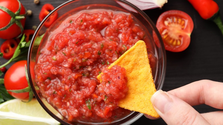 Close-up of person dipping a chip into a bowl of salsa