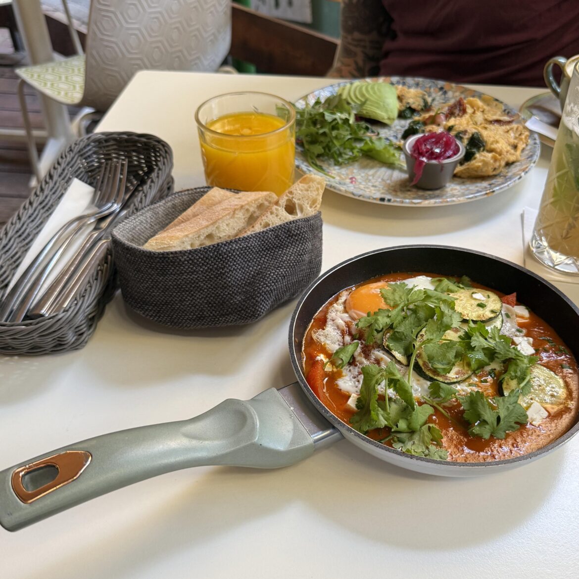 Shakshouka in Teflon with metal utensils and a side of sourdough in a cloth pouch