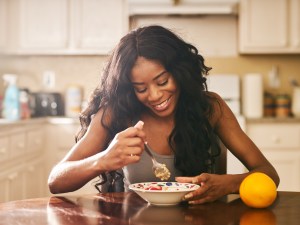 Smiling young woman eating breakfast at table in kitchen