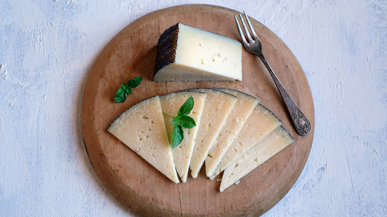 wedge and slices of manchego cheese with small fork on a round wood board