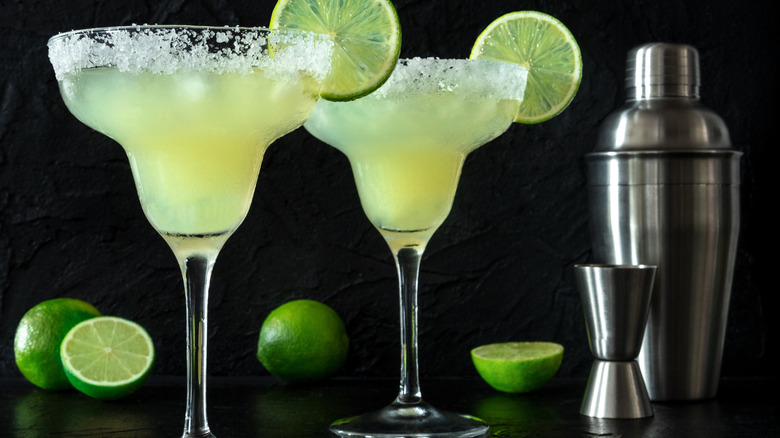 Two traditional margarita glasses with salted rims against a black background.