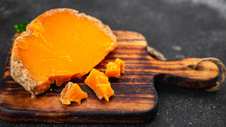 aged mimolette orange cheese on small wooden board