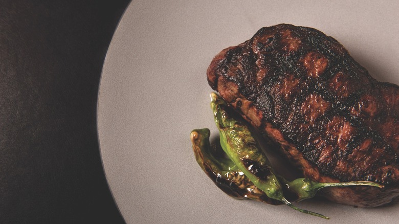 Grilled Wagyu ribeye on plate with shishito peppers