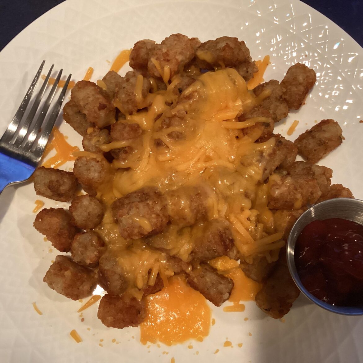 Leftover tots with shredded sharp cheddar cheese and ketchup on the side
