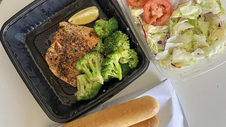 Olive Garden's herb-grilled salmon in takeout container, alongside breadsticks and salad