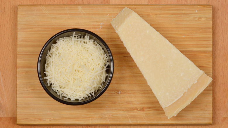 Bowl of shredded Pamesan and wedge on a wooden cutting board