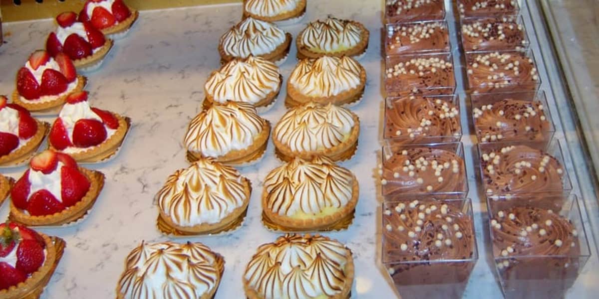 A display case at Les Halles Boulangerie-Patisserie features strawberry tarts, lemon meringue tarts with toasted tops, and cups of chocolate mousse topped with chocolate pearls, all arranged neatly on a marble countertop.