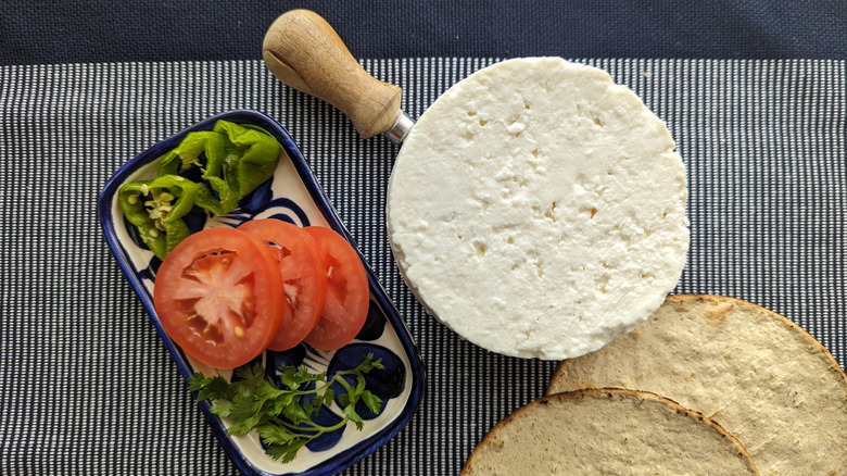 A wheel of queso panela with some salad and tortillas on the side