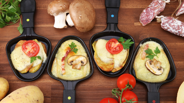 Some raclette pans with melted raclette cheese and various toppings