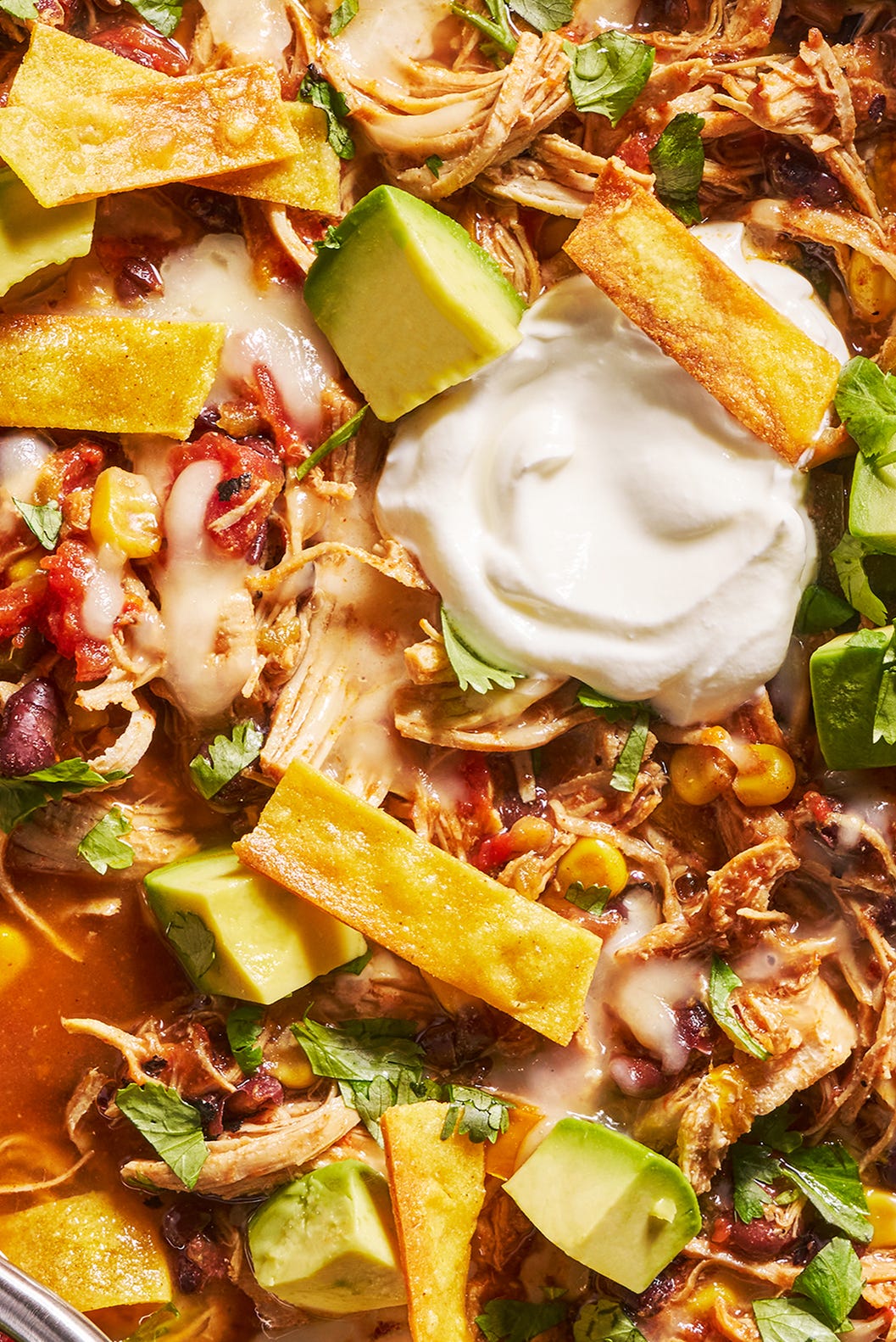 slow cooker chicken tortilla soup with sour cream, avocado slices, cheese and tortilla strips