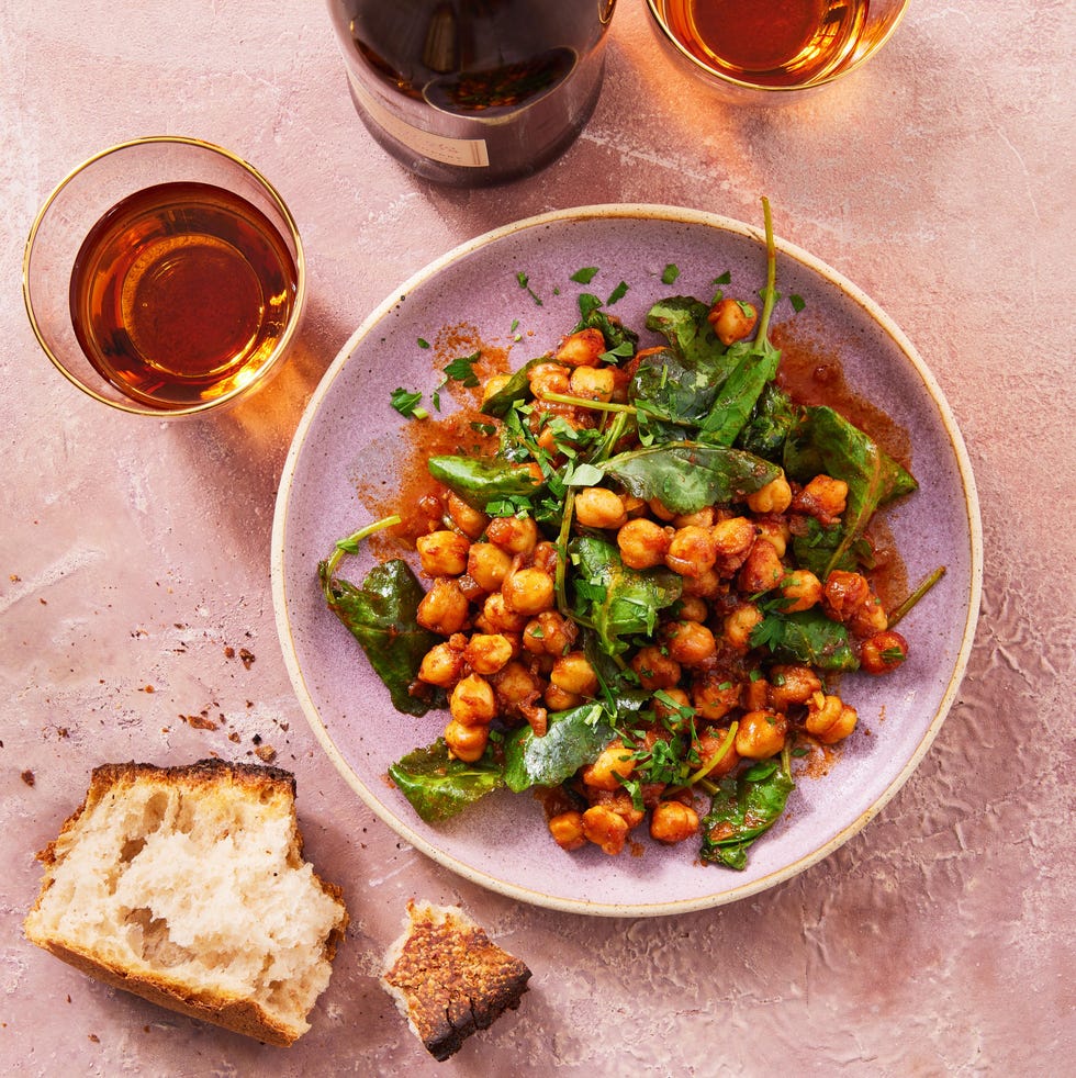 smoky glazed chickpeas and greens in a bowl with glasses of wine and torn baguette
