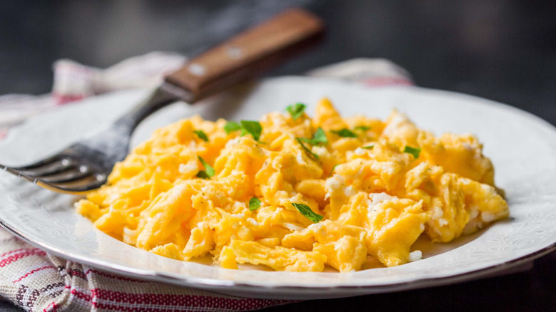 Scrambled eggs with a garnish on a white plate with a fork