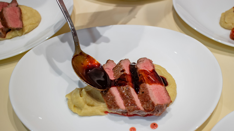 Steak served with red wine reduction over mashed potatoes on white plate