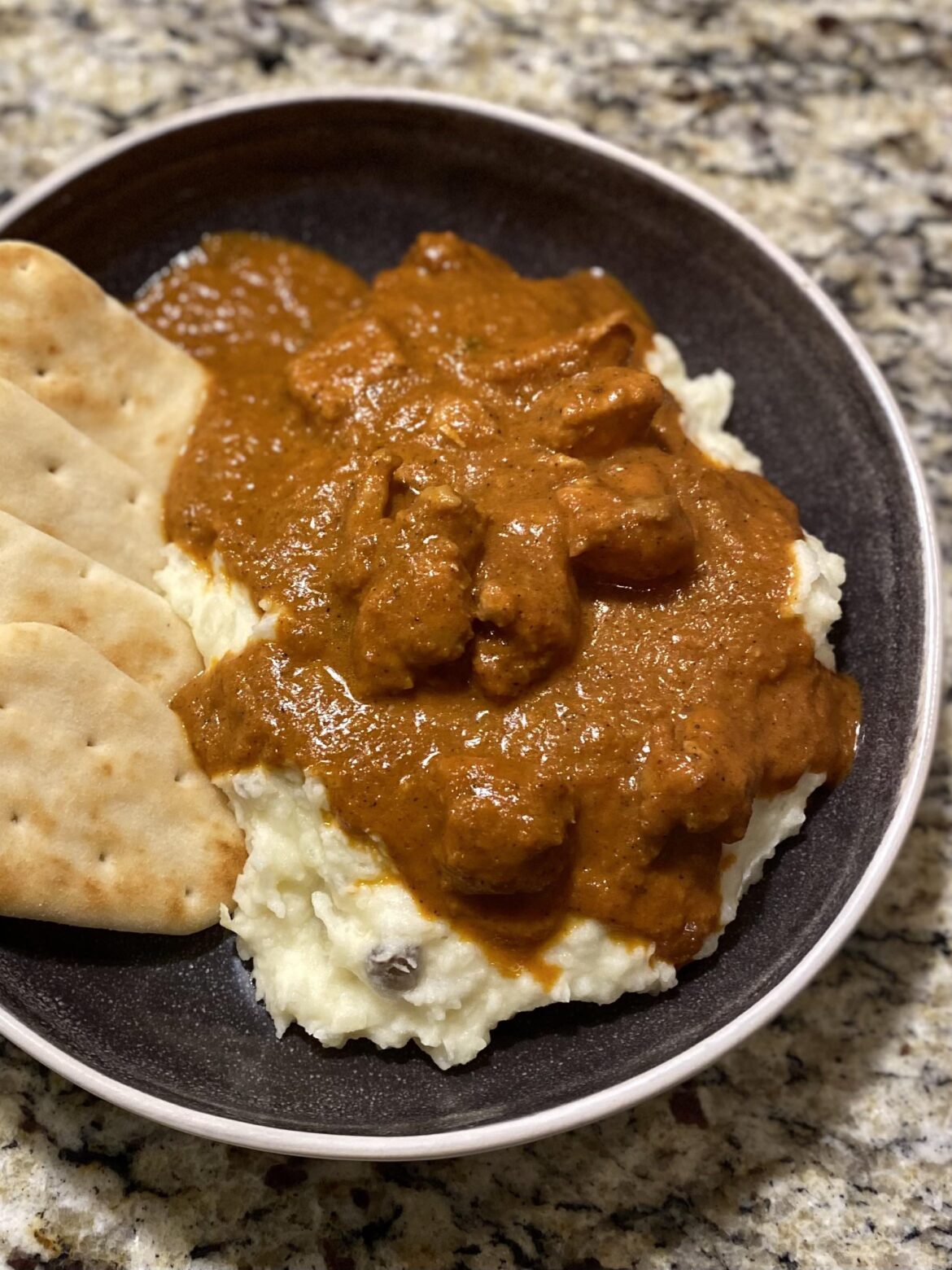 Homemade butter chicken over mashed potatoes with store-bought mini naan