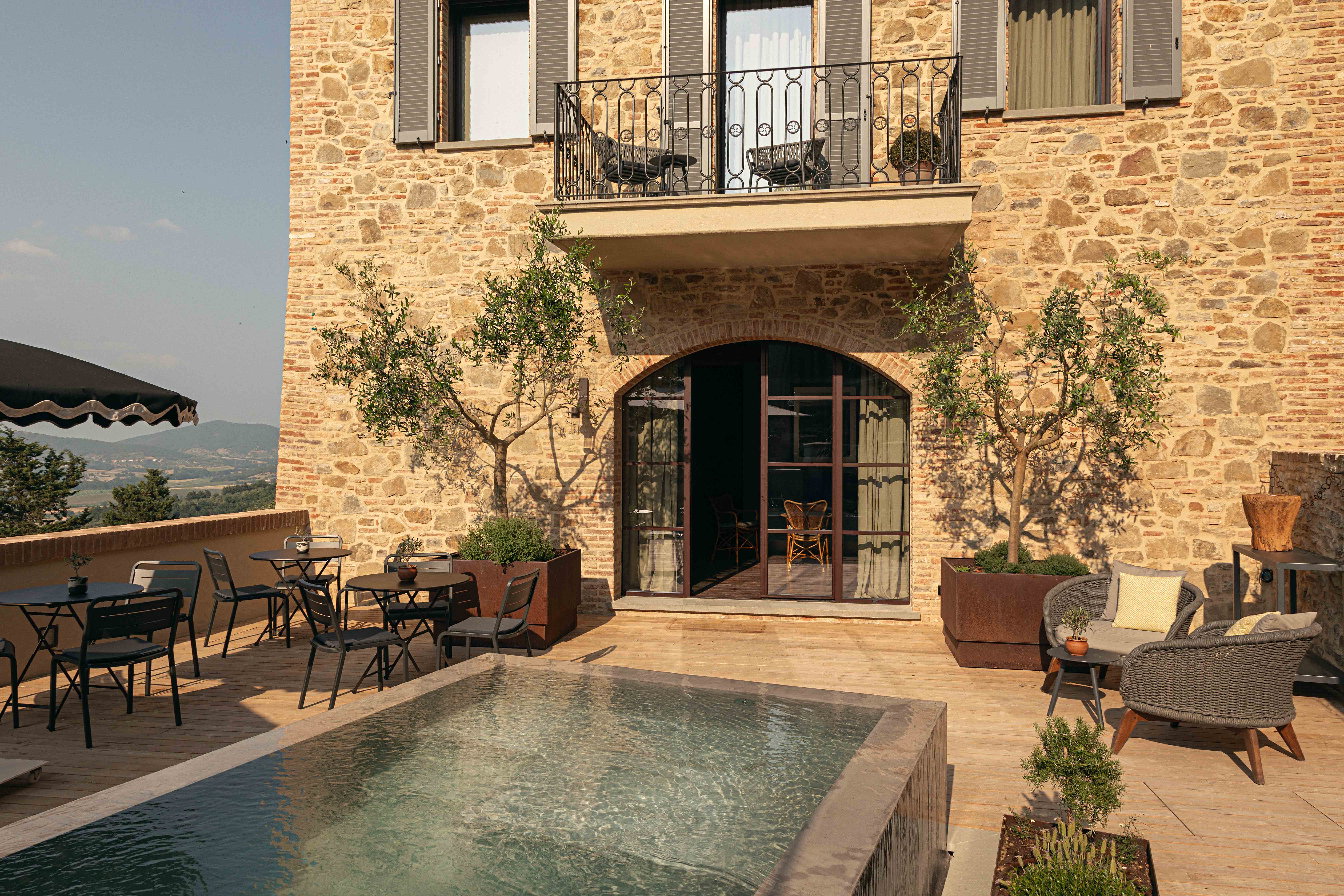 Stone building patio with plunge pool, seating area, and olive trees.