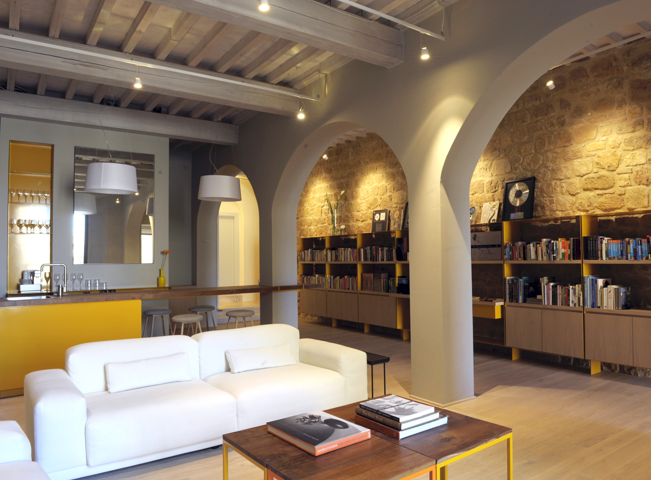 Interior view of La Bandita Townhouse in Pienza, Tuscany, showing a living area with a white sofa, yellow accents, and a library with arched alcoves.