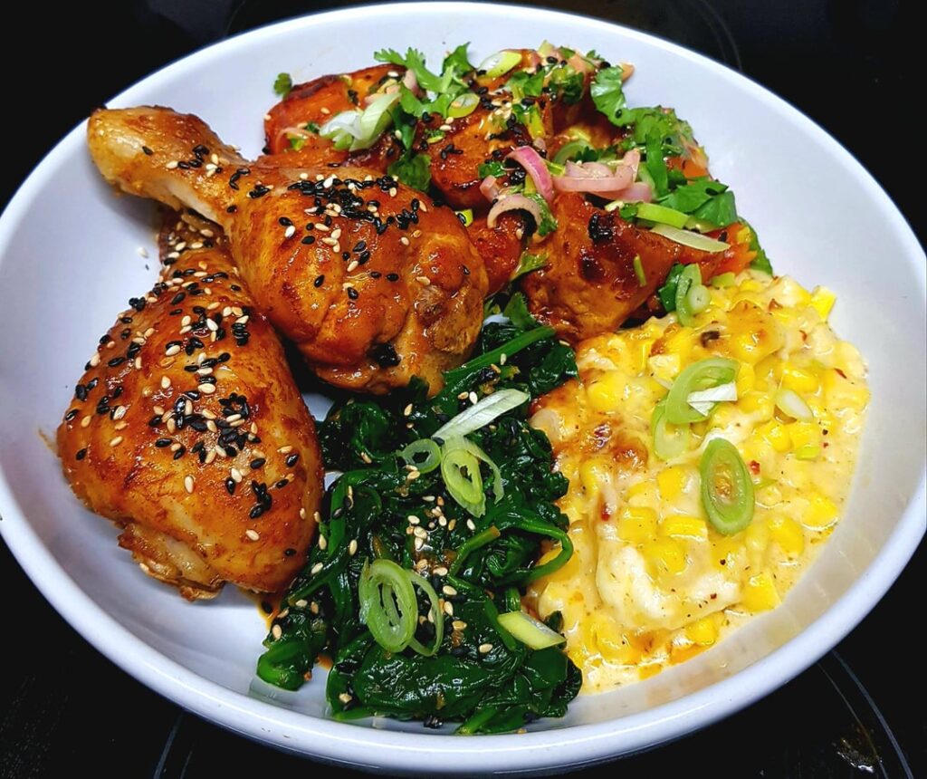 Spicy Gochujang Chicken, Roasted and Dressed Sweet Potatoes, Cheese Corn and Sesame Spinach. Garnished with Spring Onions and Coriander.