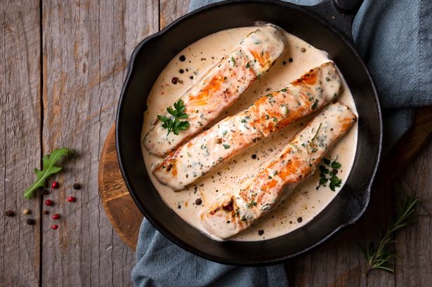 Cooked salmon fish with cream sauce in black frying pan