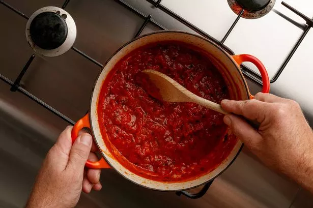 Cooking a traditional gormet tomato sauce and wooden spoon, on a stainless steal hob, shot from above