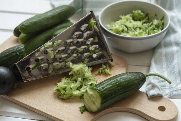 Grated and whole cucumber on cutting board