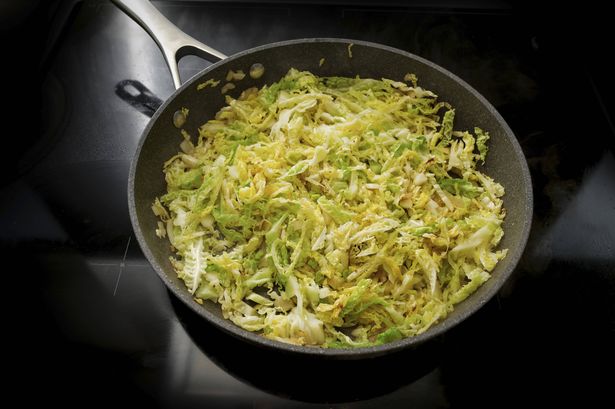 Savoy cabbage in a frying pan on the black stove, cooking at home with healthy winter vegetables, selected focus, narrow depth of field