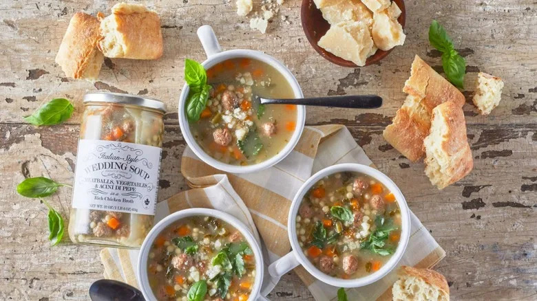 Bowls of Trader Joe's Italian wedding soup surrounded by hunks of crusty bread and Parmesan cheese