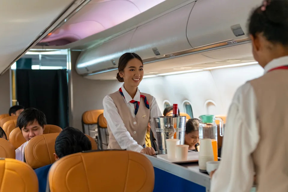 Asian woman flight attendant walking on airplane aisle serving food and drink to passenger on airplane. Cabin crew working on duty in aircraft. Airline service business and travel vacation concept.