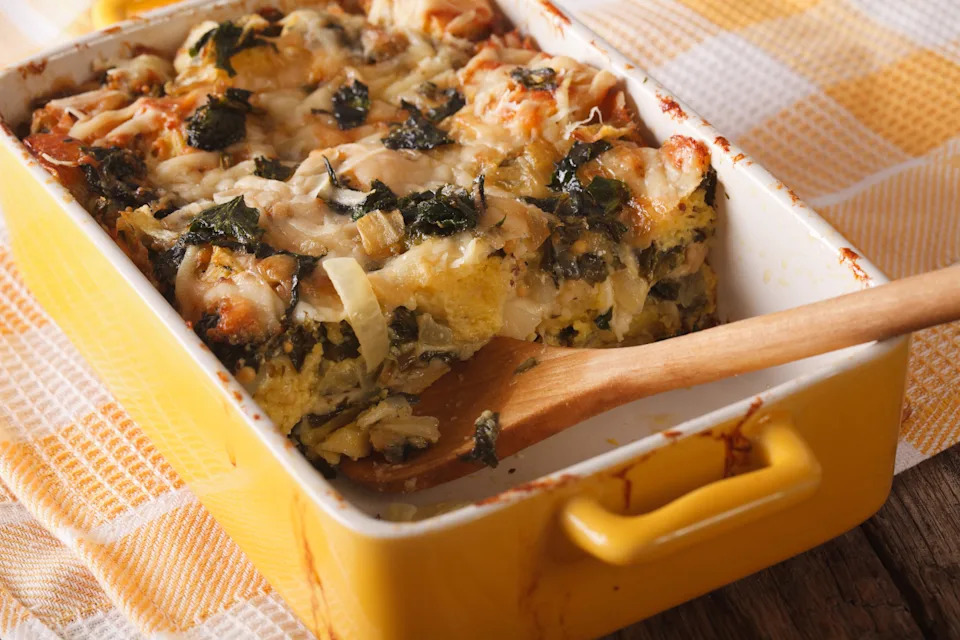 A strata or casserole with spinach, cheese and bread close up in baking dish to the table.