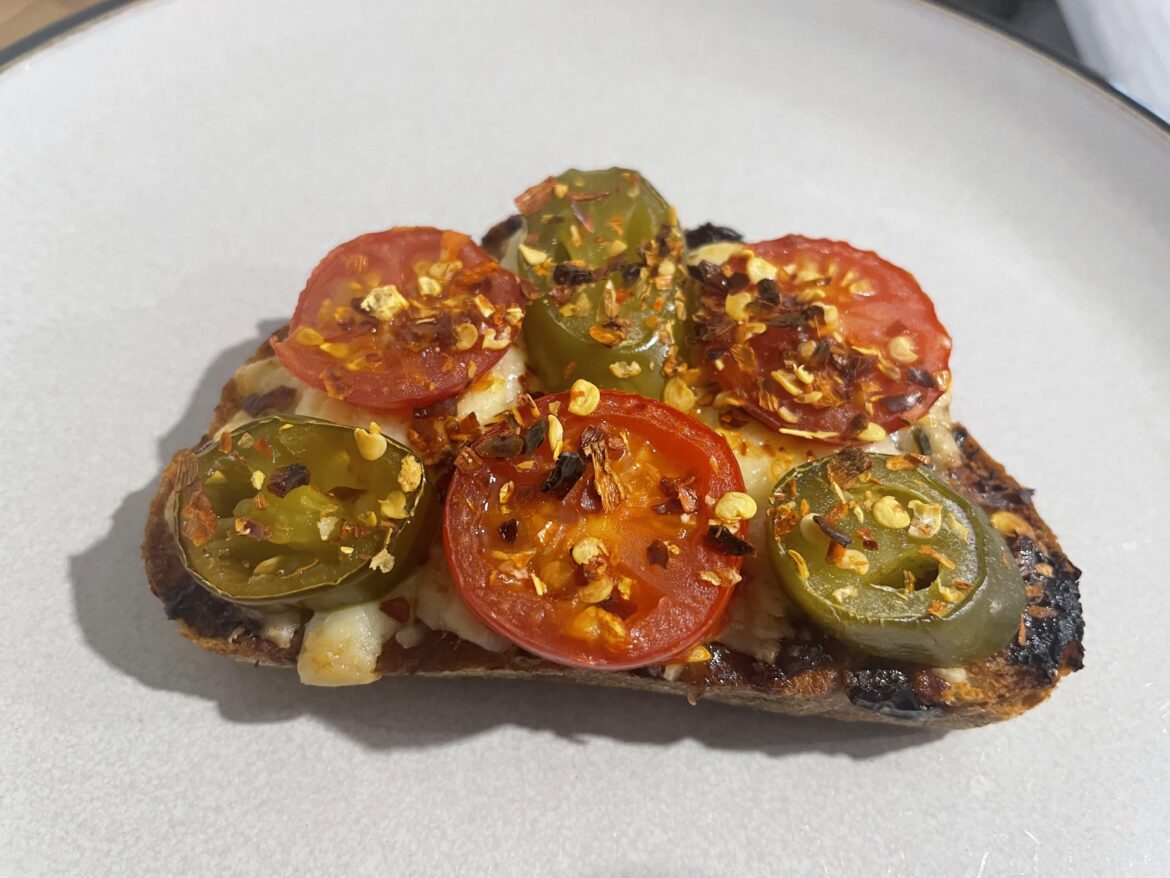 Cheese on toast using cheese & jalapeño bread with chilli jam topped with cheddar cheese, cherry tomatoes, jalapeños and chilli flakes.