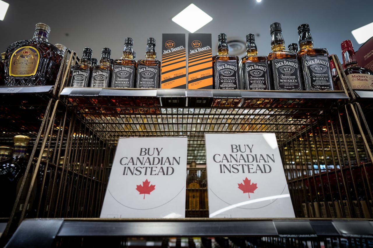 A sign that says "Buy Canadian Instead" is shown at a liquor store besides some American-made products.