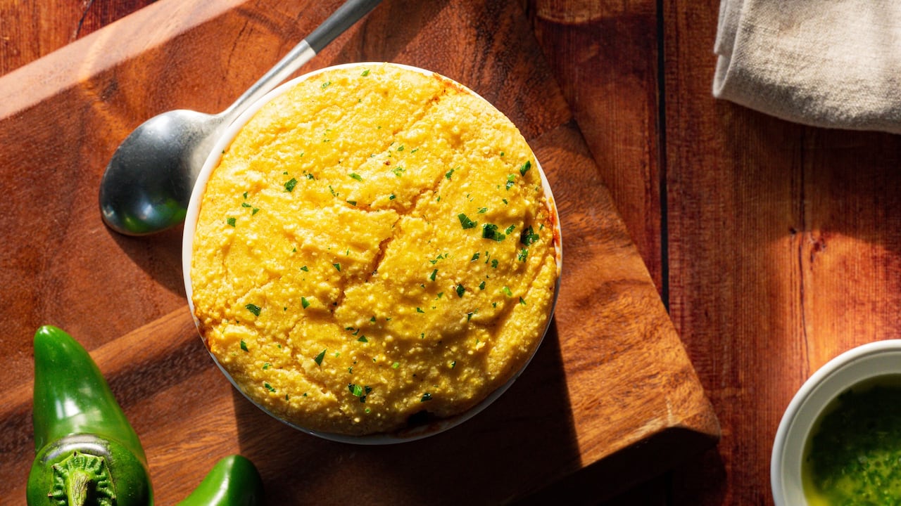 Top down shot of a round dish with chili topped with baked cornbread. It's sitting on a wooden cutting board next to jalapeño peppers.