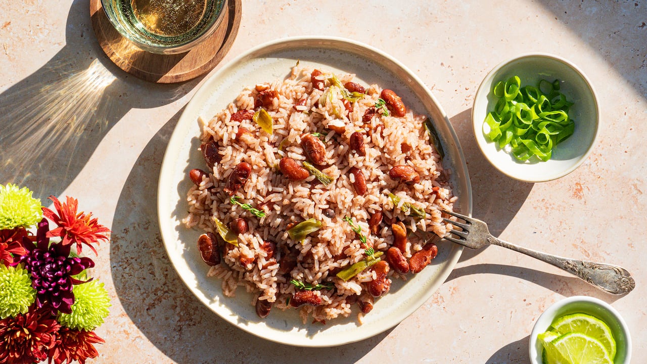 Overhead shot of a plate of rice and peas with bowls of sliced limes and green onions next to it. 