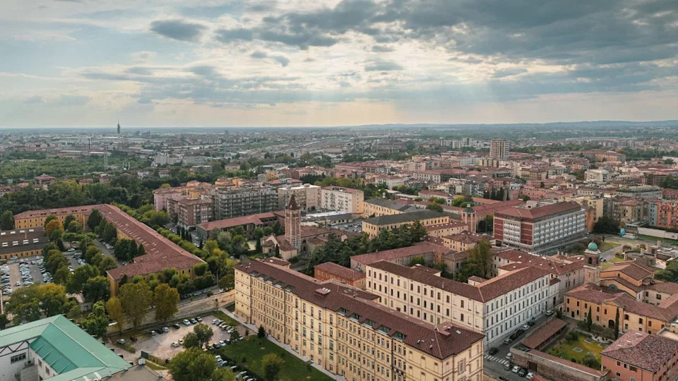 Aerial view of Modena, Italy, showcasing historic buildings and a sprawling cityscape under a cloudy sky.