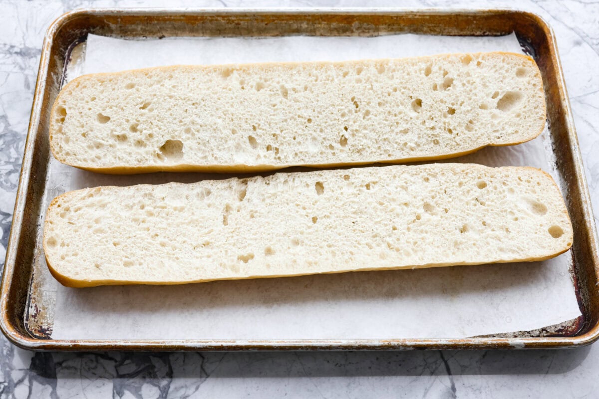 I’m not saying I’ve eaten half a loaf of this Garlic Bread straight off the baking sheet…but I’m also not not saying that. It’s golden, cheesy, dripping with garlicky butter, and so good! French bread cut in half and laying on parchment paper on a baking sheet.