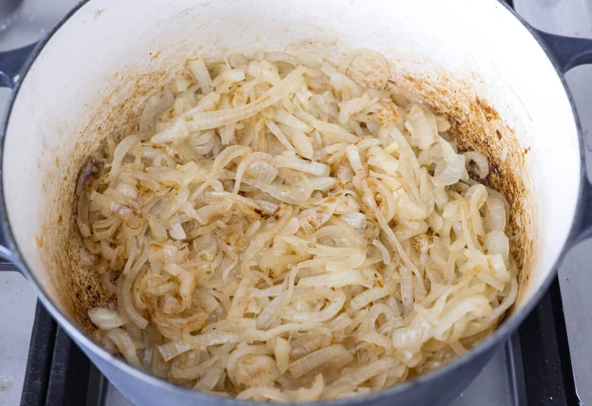 This French Onion Pot Roast is pure comfort food! Slow-cooked to perfection, the roast becomes melt-in-your-mouth tender as it simmers in a rich, savory gravy infused with the deep, caramelized flavor of onions. Overhead shot of sliced onions caramelizing in the bottom of the dutch oven.