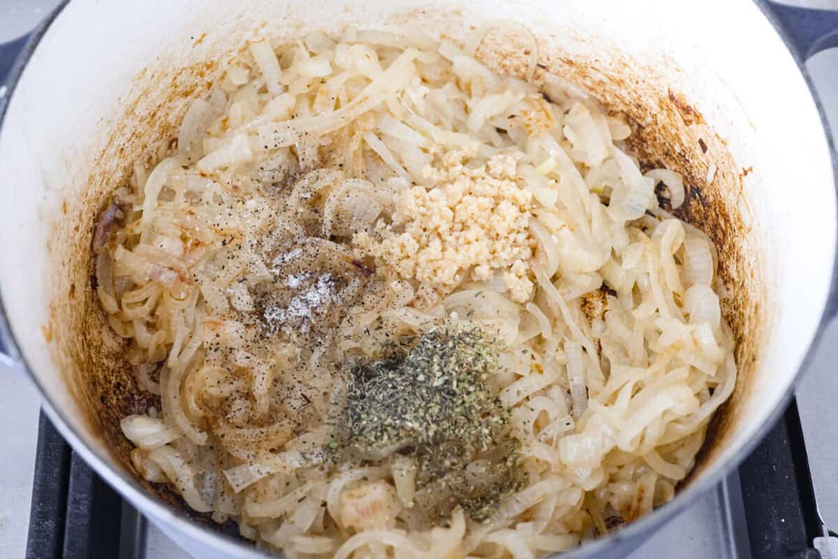 This French Onion Pot Roast is pure comfort food! Slow-cooked to perfection, the roast becomes melt-in-your-mouth tender as it simmers in a rich, savory gravy infused with the deep, caramelized flavor of onions. Overhead shot of onions with seasonings and garlic added to them.
