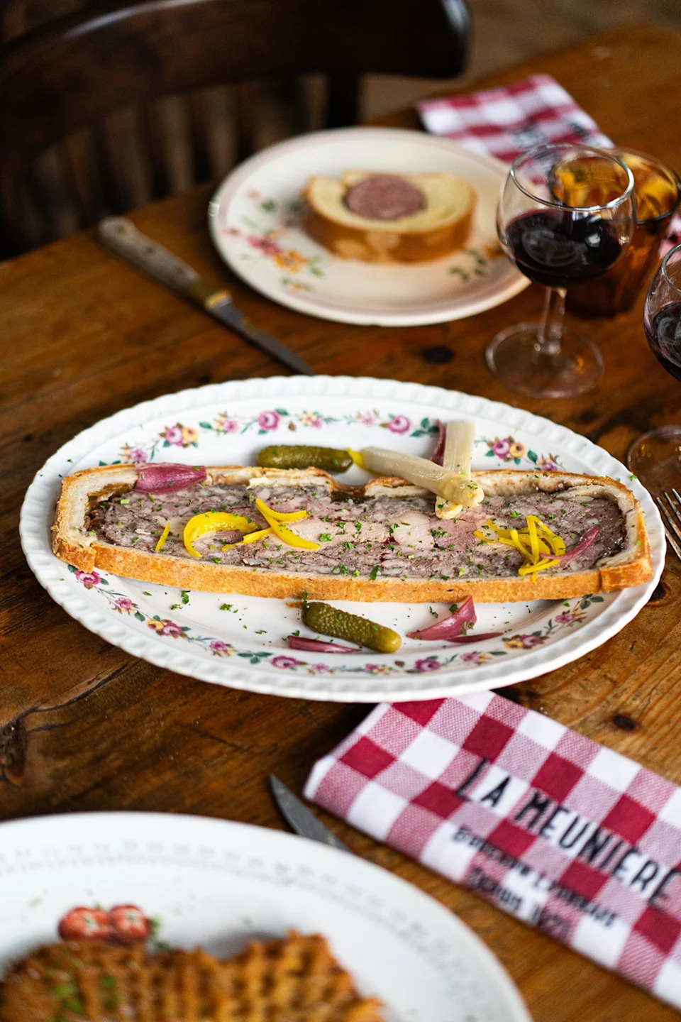 A close-up shot of a terrine topped with pickles on a rustic table with a linen napkin.