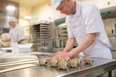 A male baker in a white outfit rolling croissants