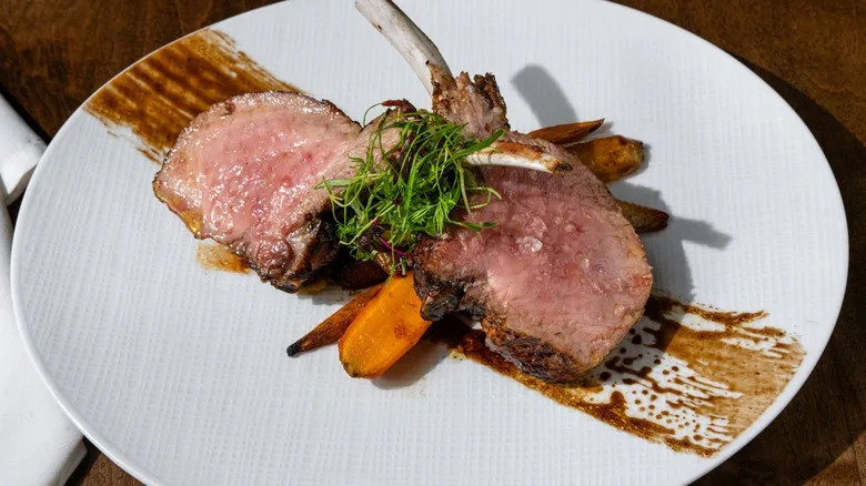 Slices of tender beef with roasted carrots, microgreens, and balsamic glaze on a white plate