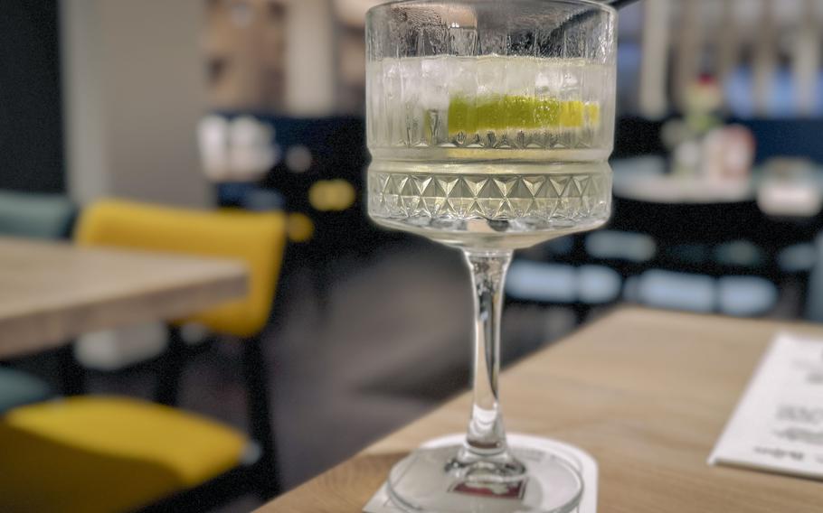 Craft cocktail with lime garnish in a geometric crystal coupe glass, served on a white coaster.