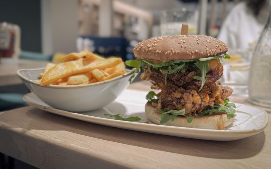 Crispy fried chicken sandwich with arugula garnish on a seeded bun, served with golden fries on a white plate