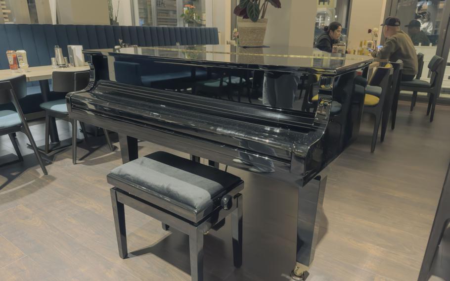  Black grand piano in a dining room surrounded by modern restaurant seating and decorative plants.