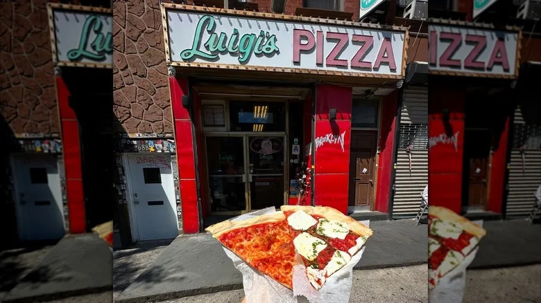 Two slices of pizza held in front of Luigi's Pizza in Brooklyn