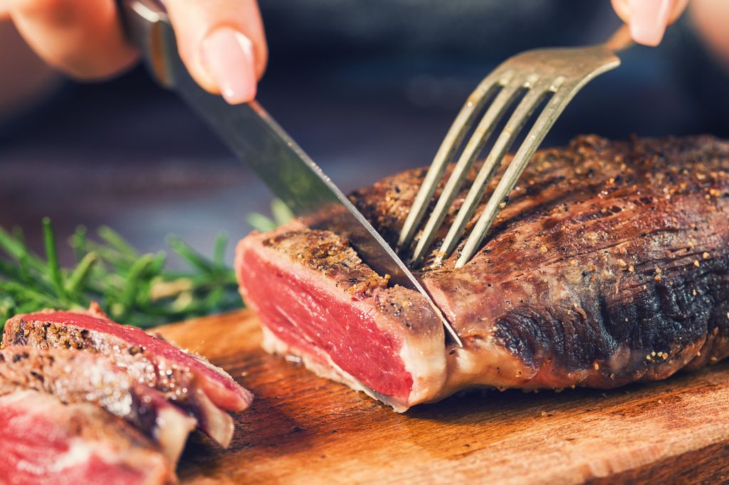 Young women cutting medium roasted beef steak on the wooden board