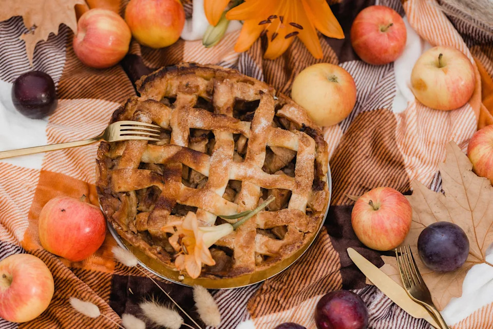An apple pie sits on a picnic blanket among apples and fall leaves