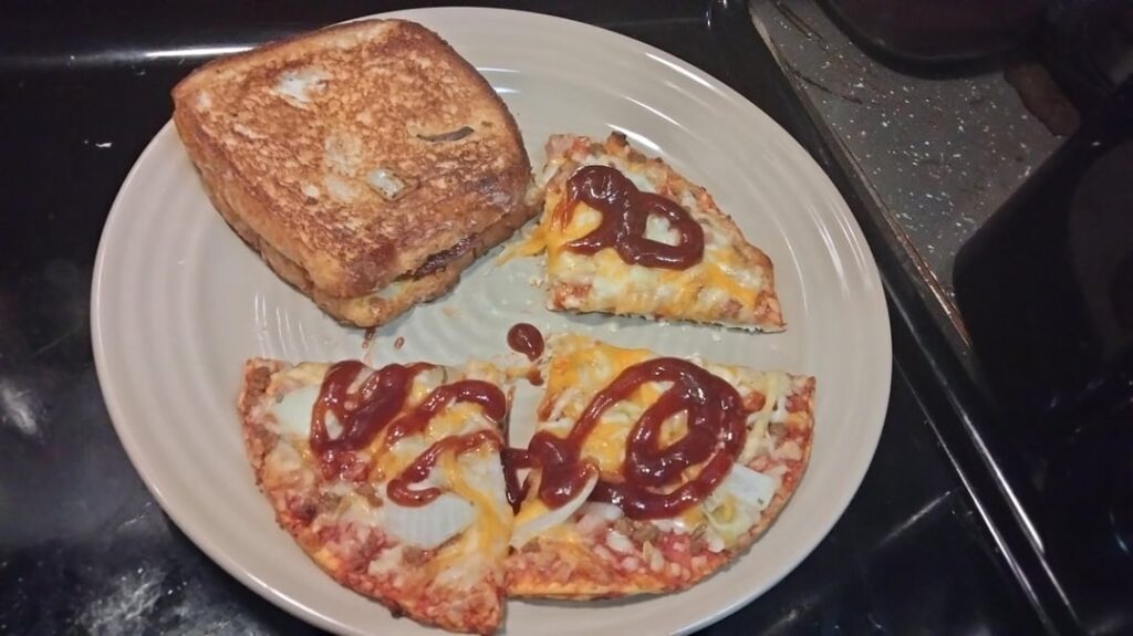 Frozen pizza with extra cheese, roasted onion and garlic, and a fried salami grilled cheese on the side.